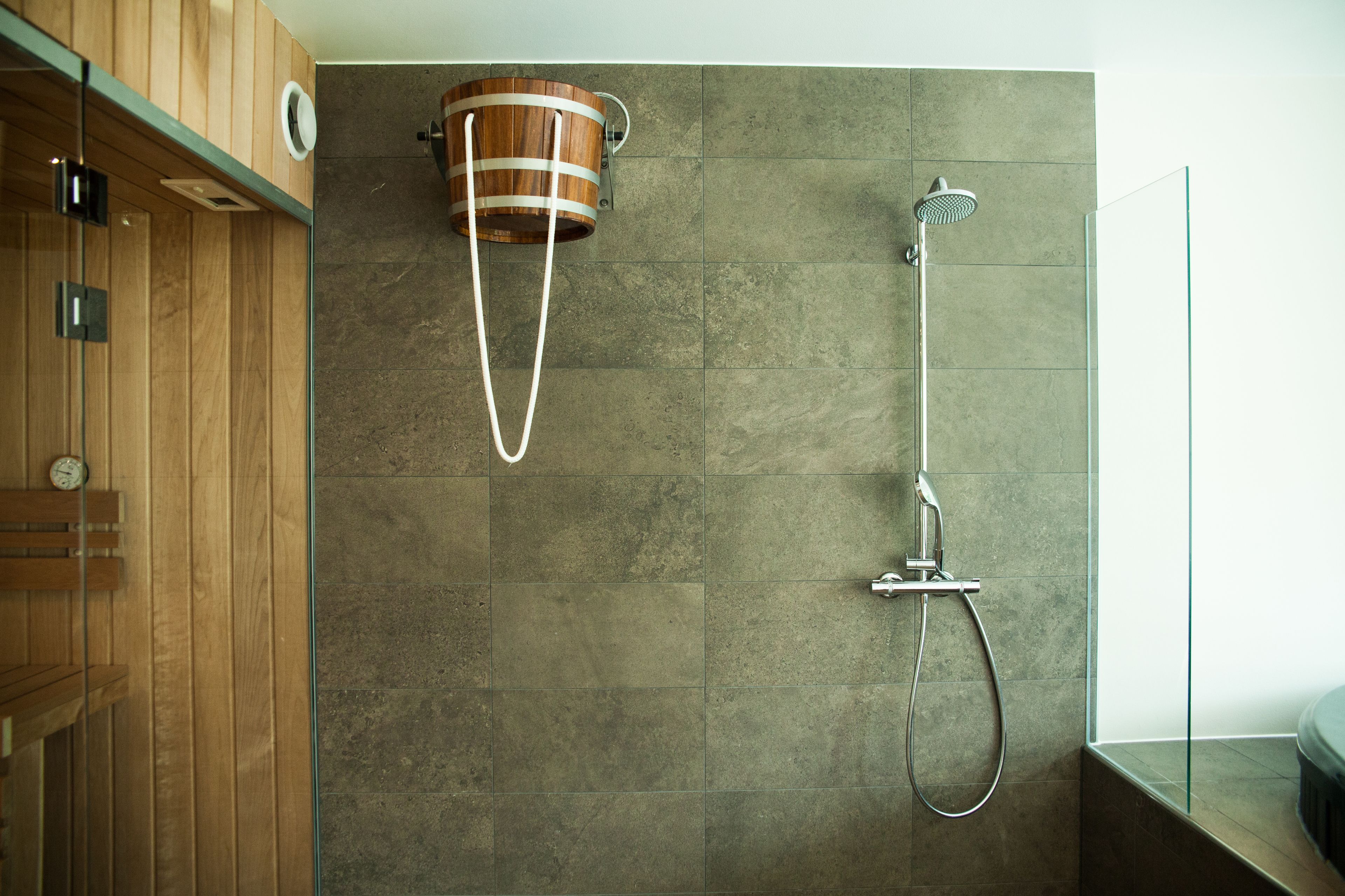 A modern bathroom with a wooden vanity, a shower with a rain showerhead, and a wooden bucket-style sink.