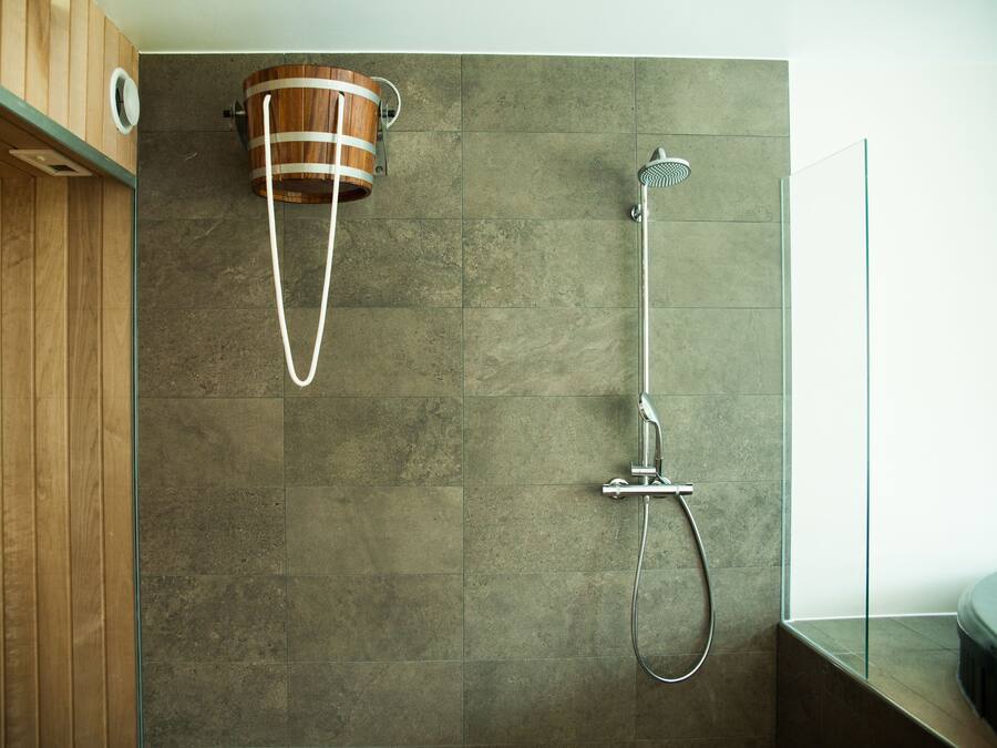 A modern bathroom with a wooden vanity, a shower with a rain showerhead, and a wooden bucket-style sink.