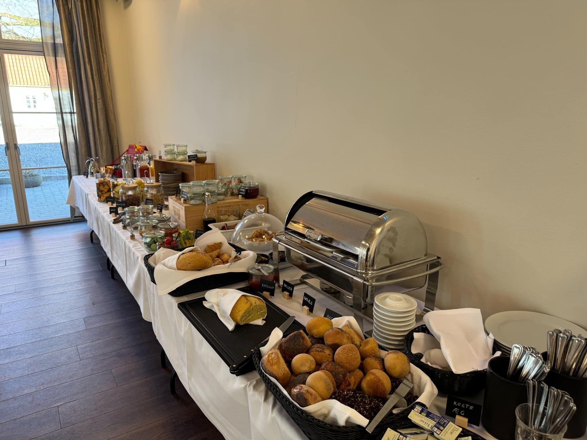 A buffet setup with various food items, including breads and pastries, and a self-service hot food station.