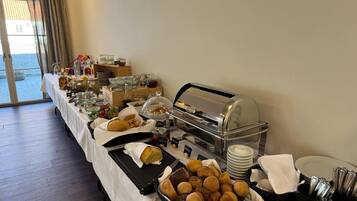 A buffet setup with various food items, including breads and pastries, and a self-service hot food station.