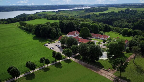 An aerial view of a large estate with a main building surrounded by lush green fields and a lake in the background.