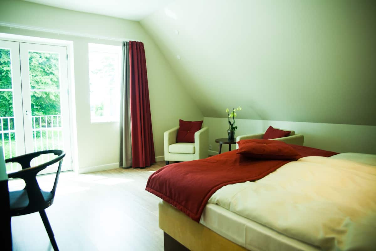 A bedroom with a bed, two chairs, a small table, and a window with curtains.