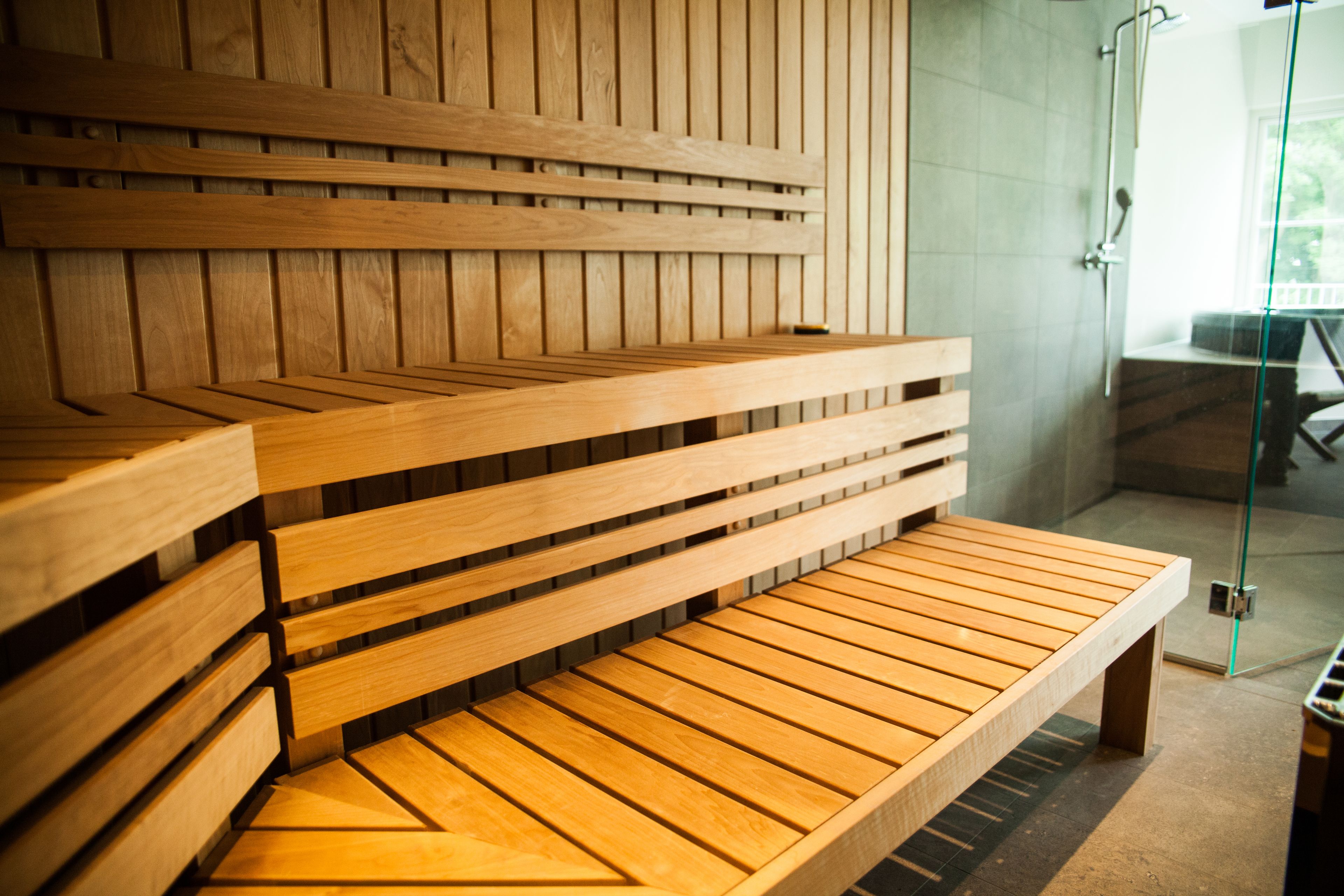 A wooden bench with a slatted design, positioned in a room with a glass door leading to an outdoor area.