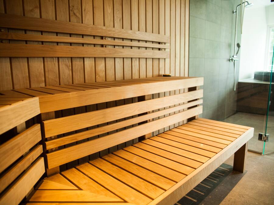 A wooden bench with a slatted design, positioned in a room with a glass door leading to an outdoor area.