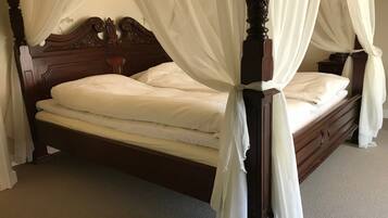 A four-poster canopy bed with white linens, wooden headboard, and a nightstand with a lamp.