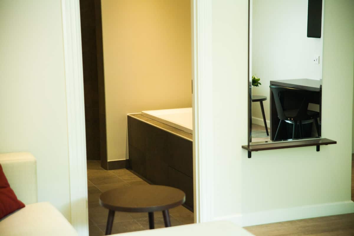 A modern bathroom with a white toilet, a small round stool, and a mirror above a dark wooden vanity.