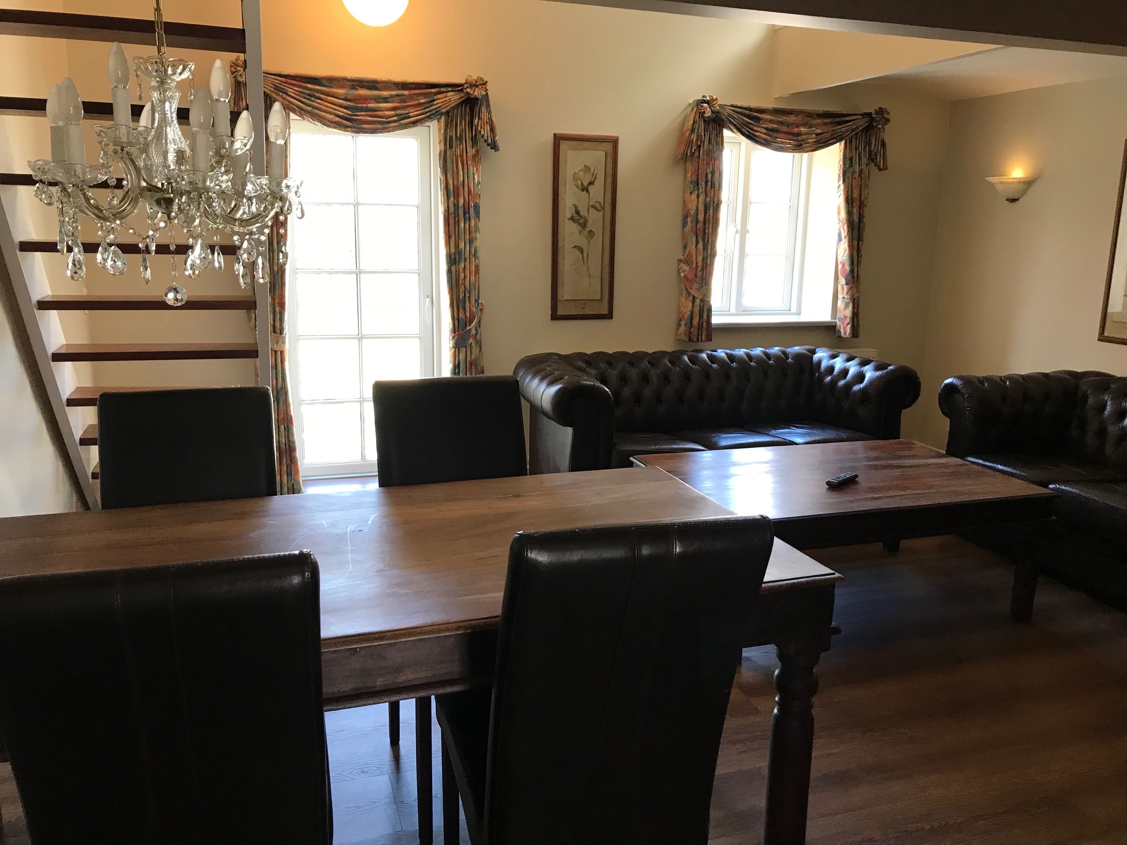 A dining area with a wooden table, black leather sofa, and a chandelier.