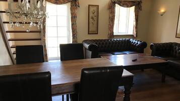 A dining area with a wooden table, black leather sofa, and a chandelier.