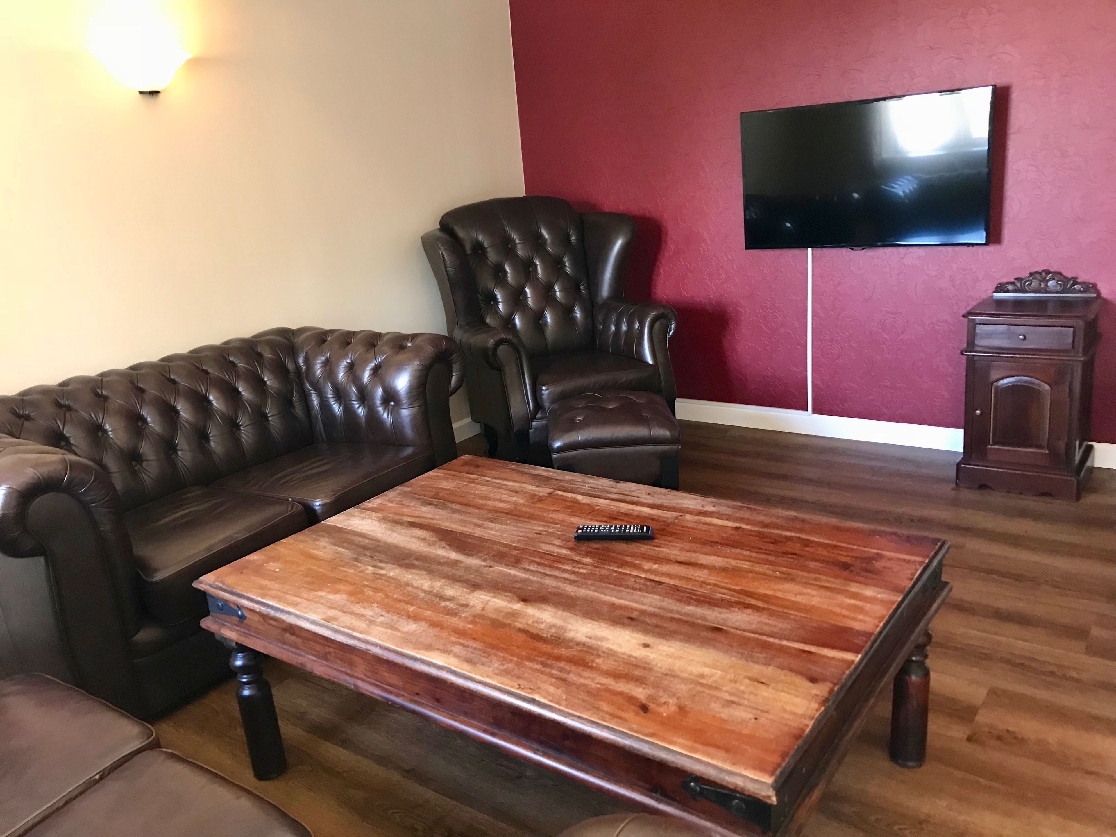 Una sala de estar con un sofá de cuero, una mesa de centro de madera, un sillón de cuero, un televisor montado en la pared y un mueble bajo de madera.