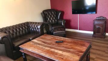 Una sala de estar con un sofá de cuero, una mesa de centro de madera, un sillón de cuero, un televisor montado en la pared y un mueble bajo de madera.