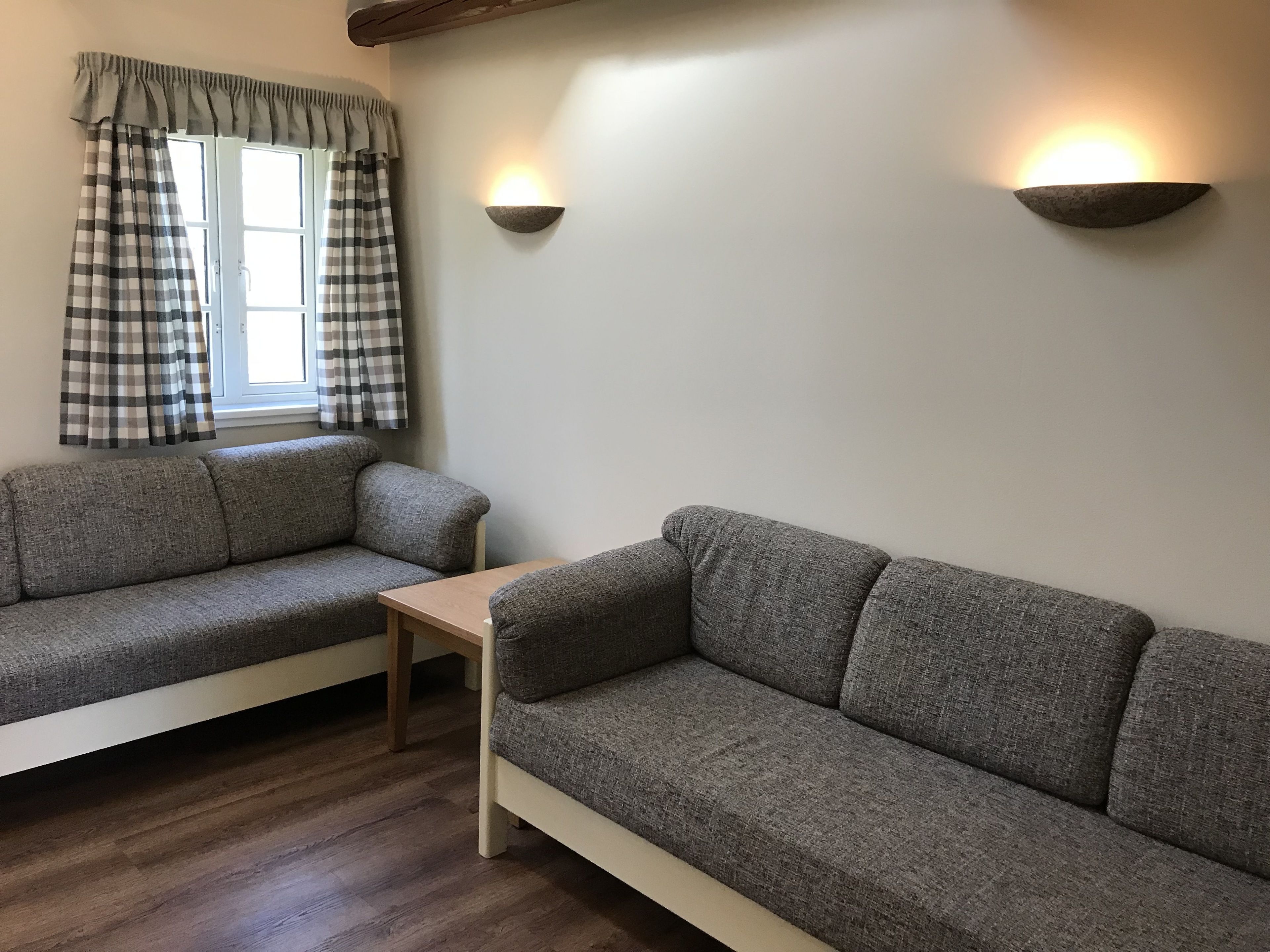 En hyggelig stue med to grå sofaer, et træbord og et vindue med ternede gardiner.