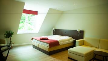 A bedroom with a bed, a sofa, a chair, a window, and a plant.