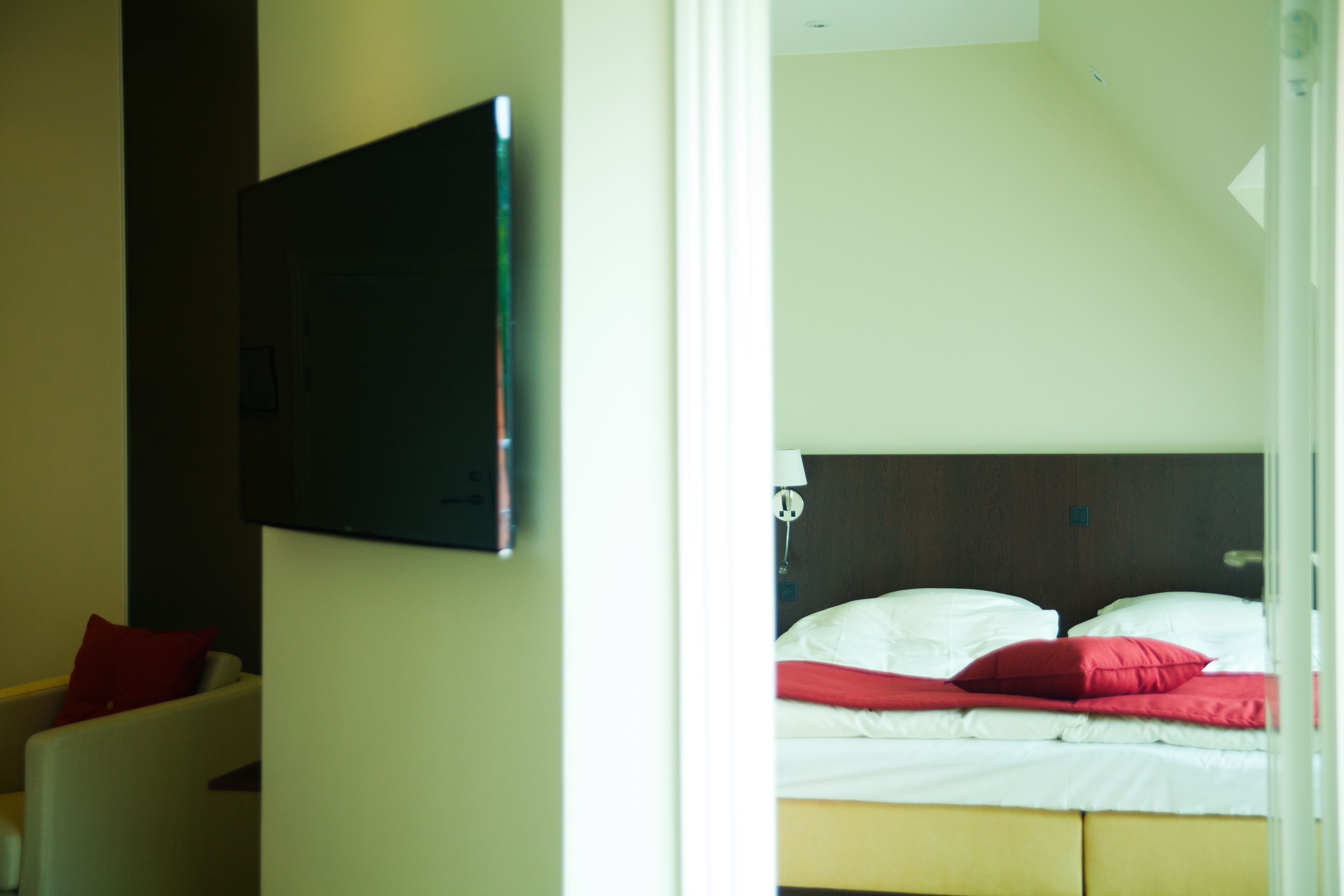Habitación de hotel con una cama, un televisor montado en la pared y una silla con un cojín rojo.