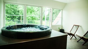 A hot tub in a room with large windows, a chair, and a potted plant. - Hotel BramslevGaard (Hobro)