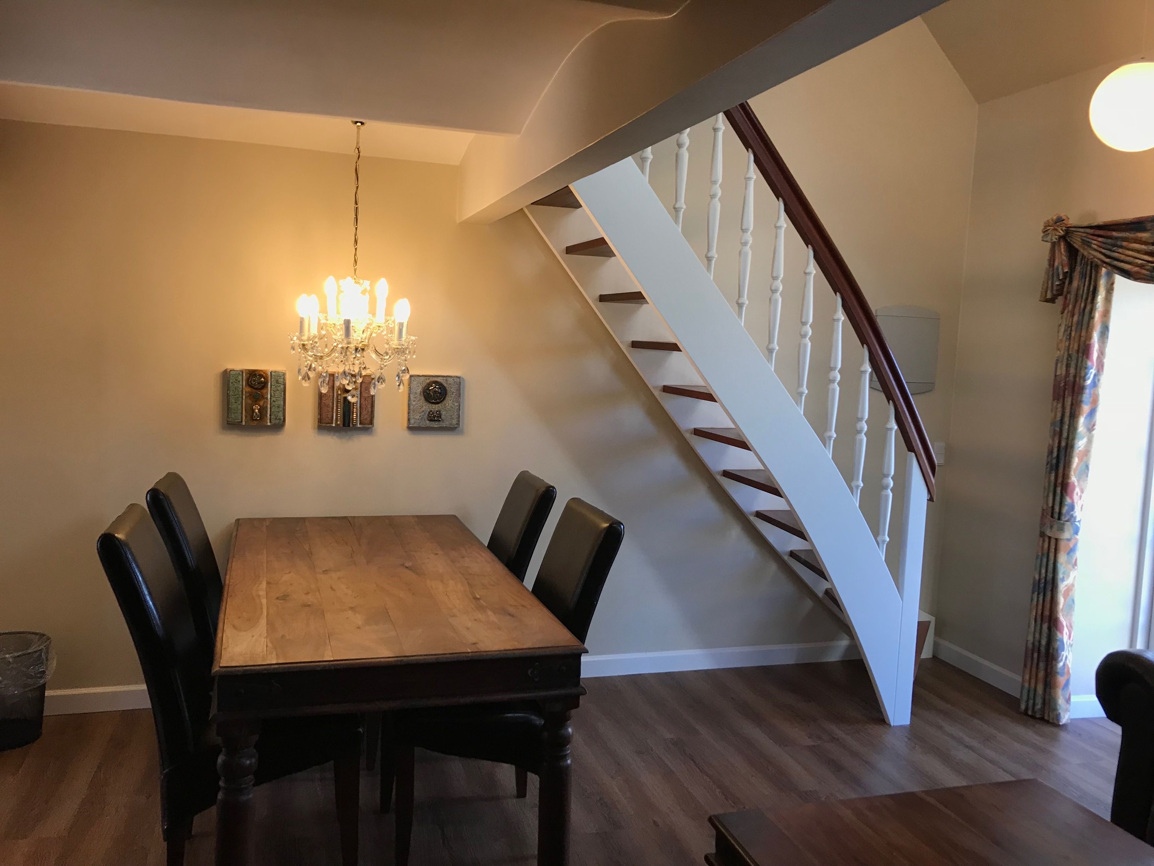 A dining area with a wooden table and chairs, a chandelier, and a staircase with white balusters.