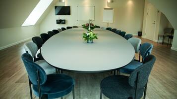 Ein Konferenzraum mit rundem Tisch, Stühlen, einer Blumenvase und einem Fernseher an der Wand.