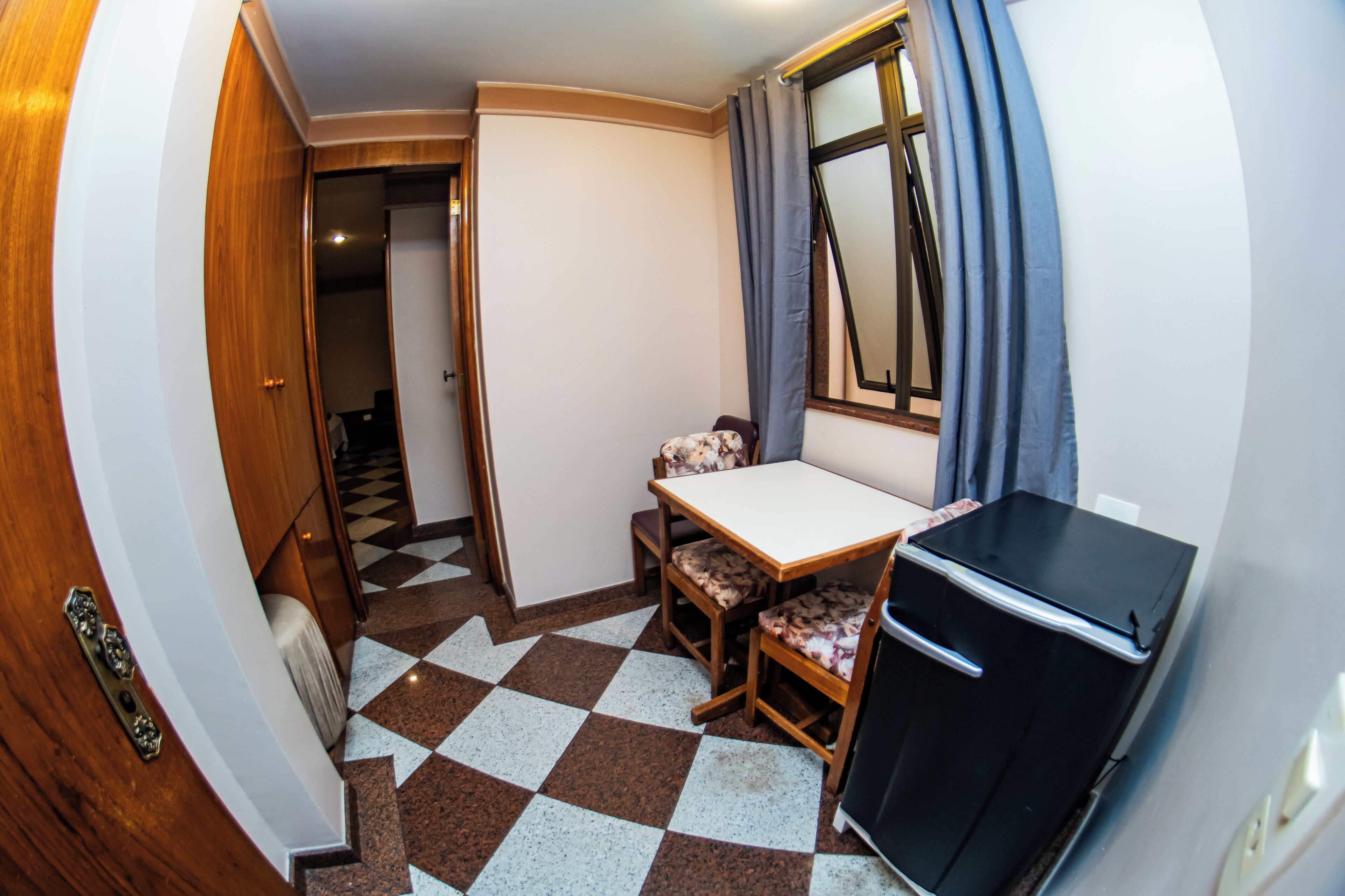 A compact kitchen with a checkered floor, a small dining table, and a refrigerator.