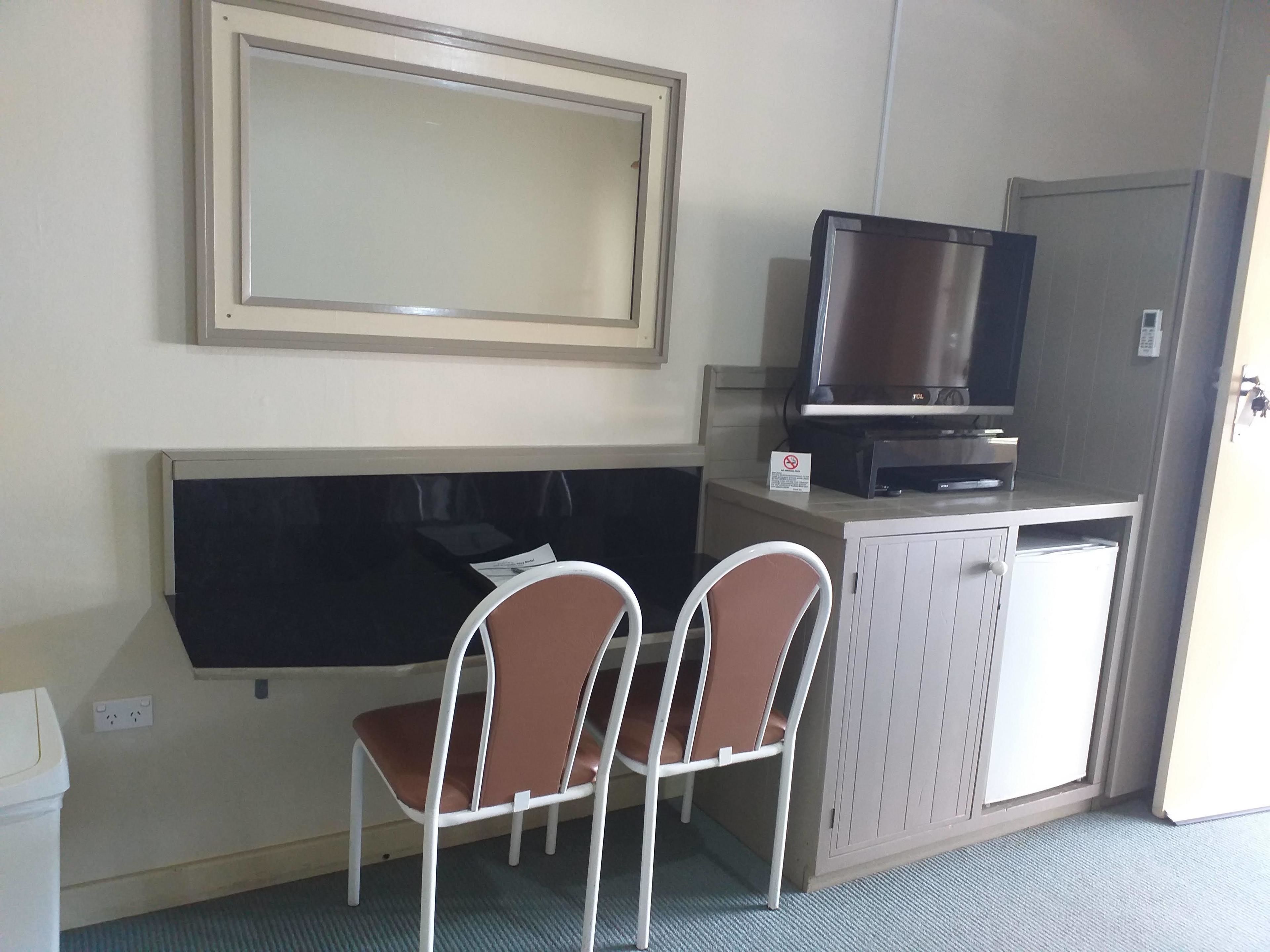Ein kleines Zimmer mit Fernseher auf einem Schrank, zwei Stühlen und einem großen Spiegel an der Wand.