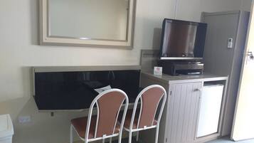 Ein kleines Zimmer mit Fernseher auf einem Schrank, zwei Stühlen und einem großen Spiegel an der Wand.