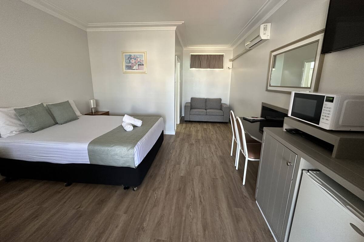 A hotel room with a bed, a desk with a microwave, a chair, and a small refrigerator.
