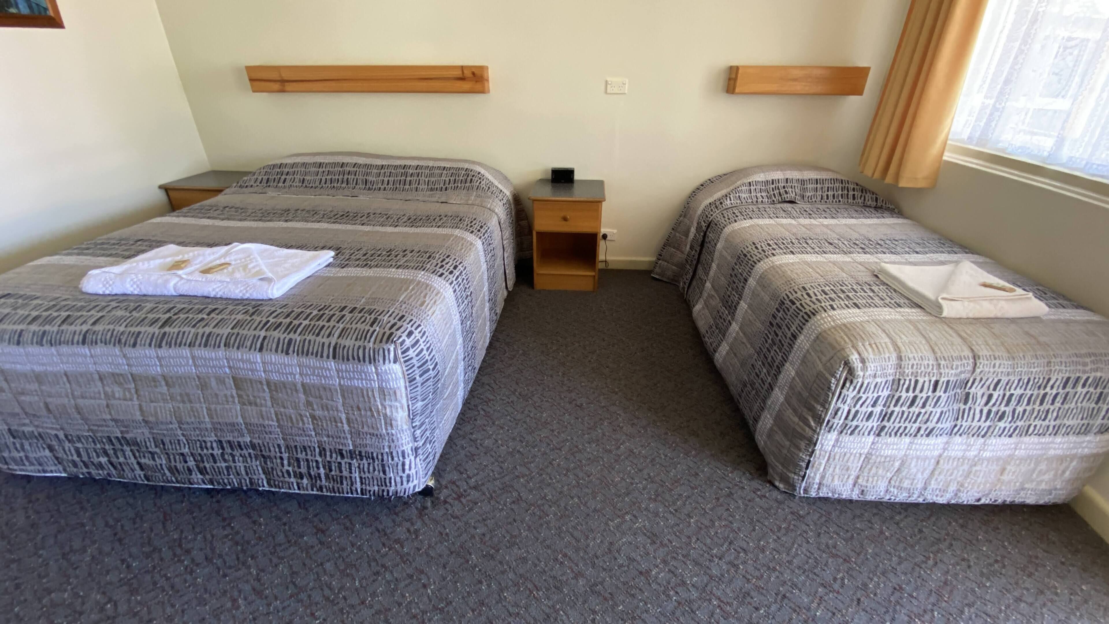 A hotel room with two beds, a small wooden nightstand, and a window with curtains.