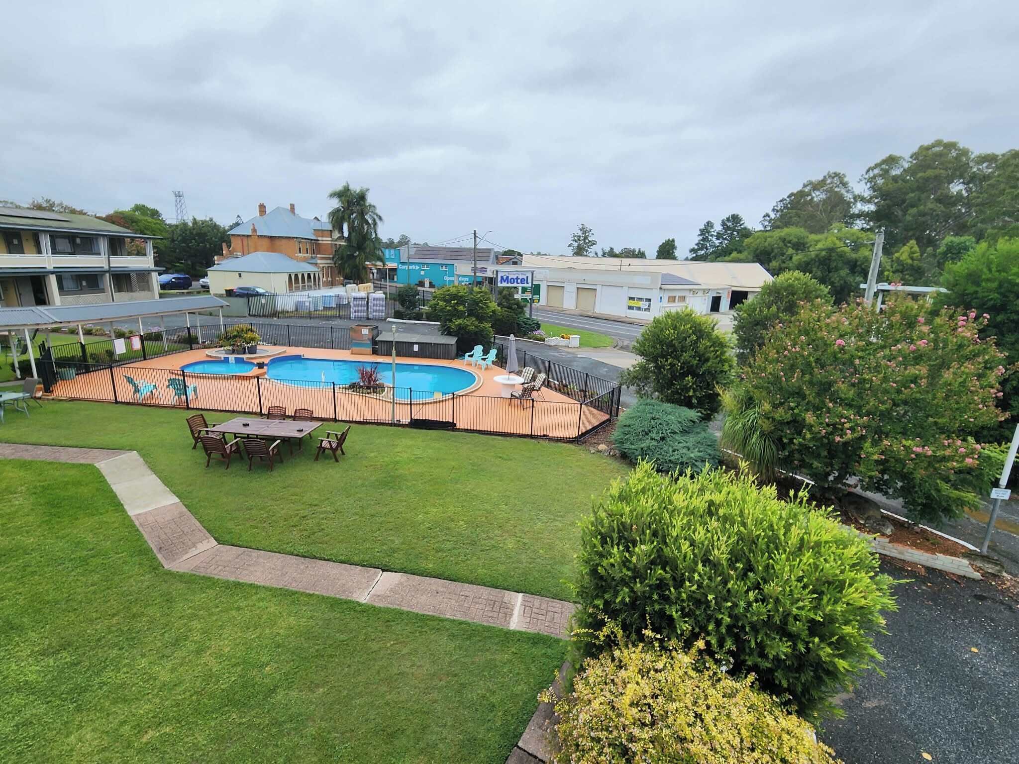 A hotel with a swimming pool, outdoor seating area, and a well-maintained lawn.
