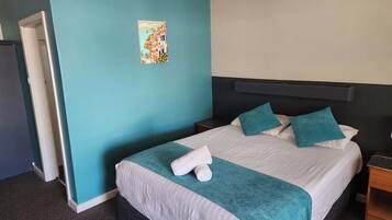A hotel room with a bed, a nightstand, a painting on the wall, and a door to the left.