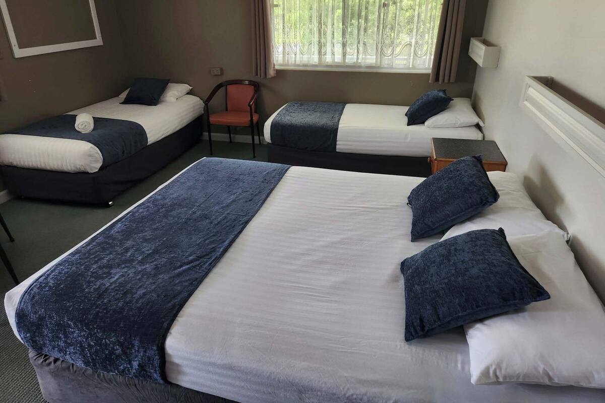 A hotel room with two single beds and one double bed, all with blue bedding. There is a chair and a small table in the room.