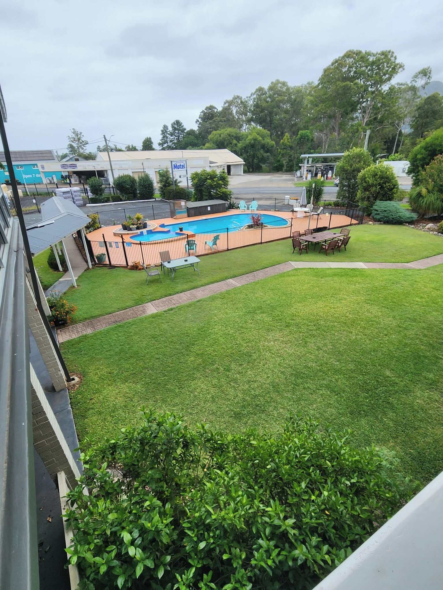 A hotel with a swimming pool, a fenced patio area, and a well-maintained lawn.