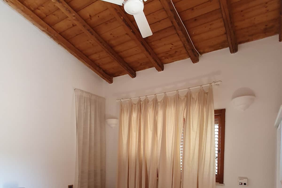 Une chambre à coucher avec un lit, des rideaux, un ventilateur de plafond et un sol carrelé.