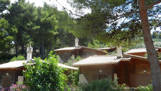 A row of wooden cabins with tiled roofs, surrounded by dense trees and greenery. - Tenuta Molino di Mare - Ecoresort with Villini (Rodi Garganico)