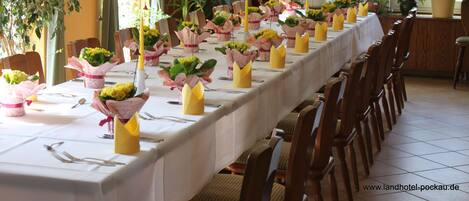 A long dining table with yellow vases of flowers and candles, surrounded by wooden chairs.