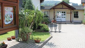 A building with a tiled roof, a signboard, and a paved driveway leading to a white car parked in front. - Landhotel Pockau (Lengefeld)