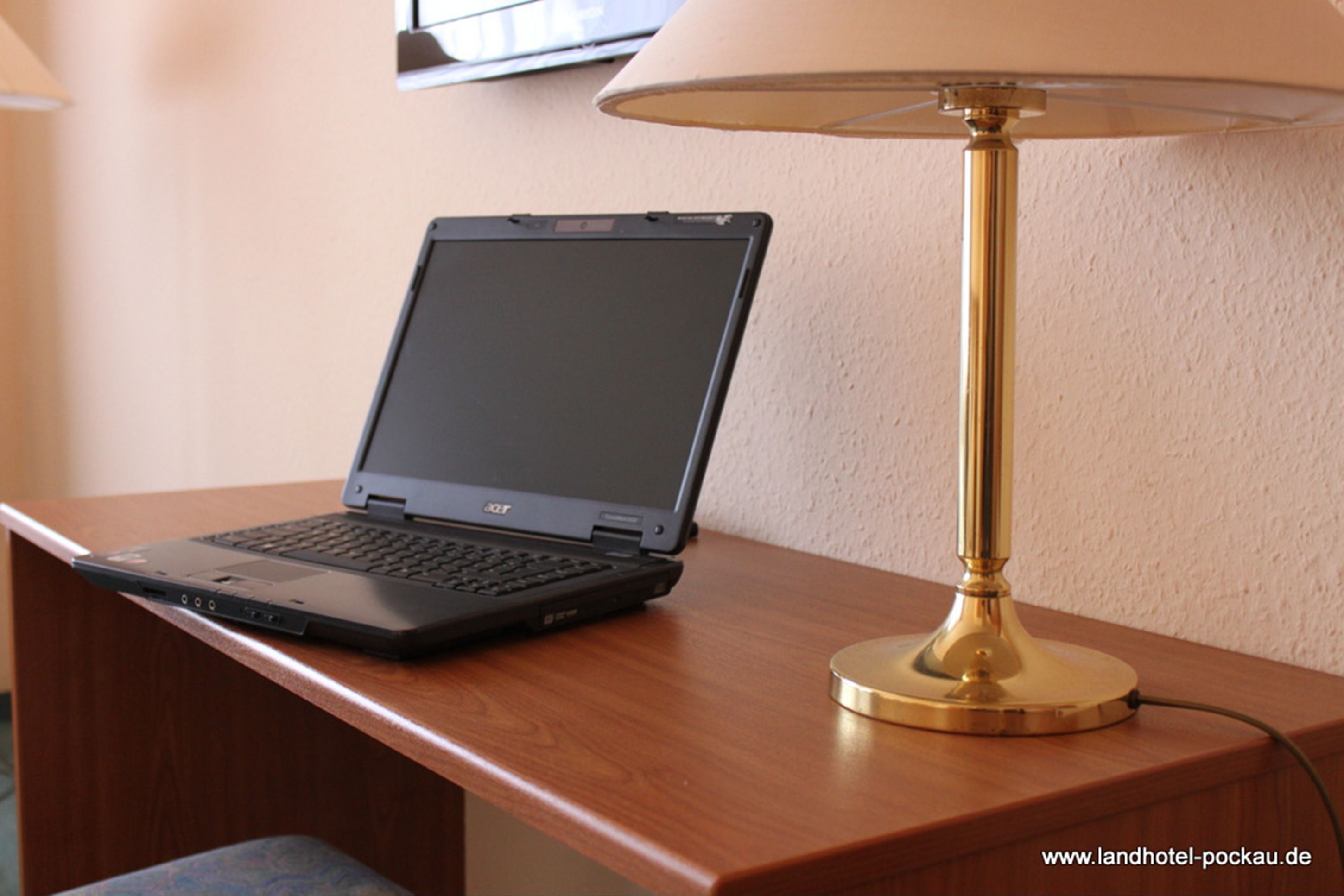 Een laptop op een houten bureau met een messing lamp ernaast.