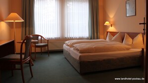 A hotel room with a double bed, two chairs, a desk, and a window with curtains. - Landhotel Pockau (Lengefeld)