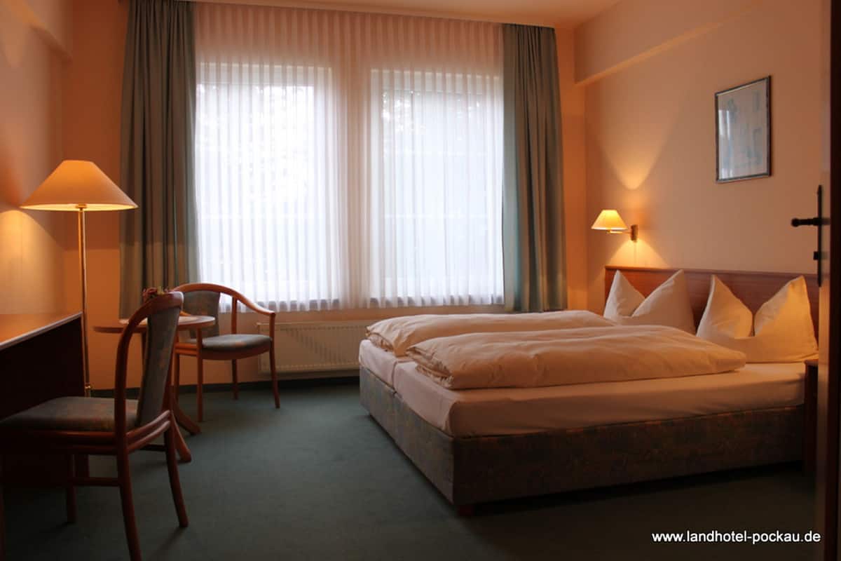 A hotel room with a double bed, two chairs, a desk, and a window with curtains.
