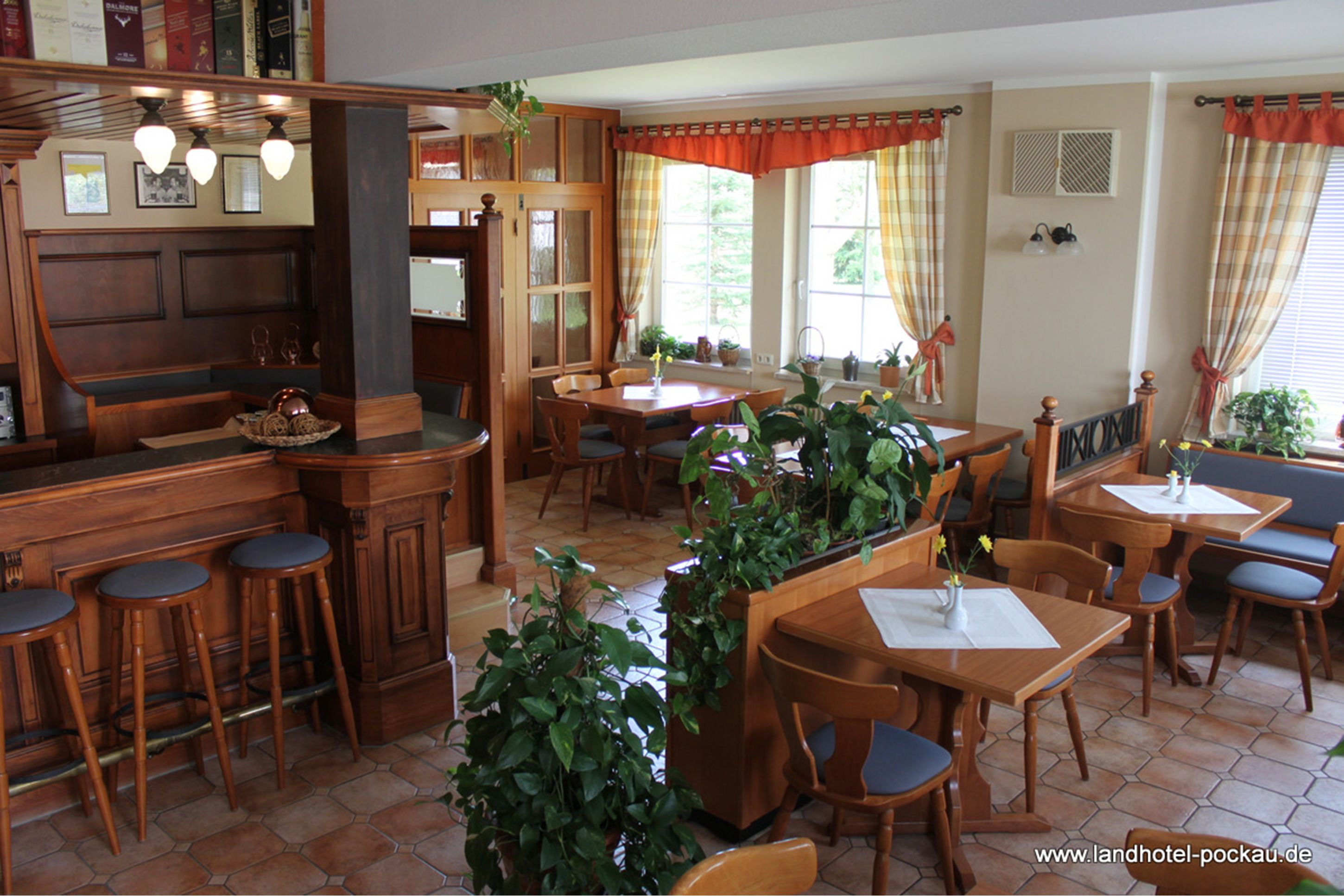 A cozy restaurant with wooden furniture, a bar area, and potted plants.