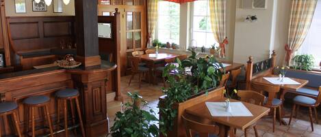 A cozy restaurant with wooden furniture, a bar area, and potted plants.