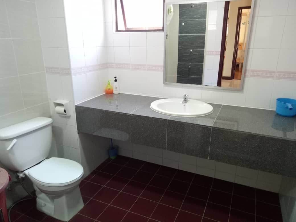 Une salle de bain avec des toilettes blanches, un lavabo surmonté d’un miroir et un sol carrelé de carreaux rouges.
