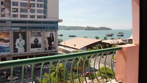 A view from a balcony overlooking a busy street with boats on the water, a distant island, and a building with advertisements. - Jack's CondoApartment @ Marina Court Resort Condominium (Kota Kinabalu)
