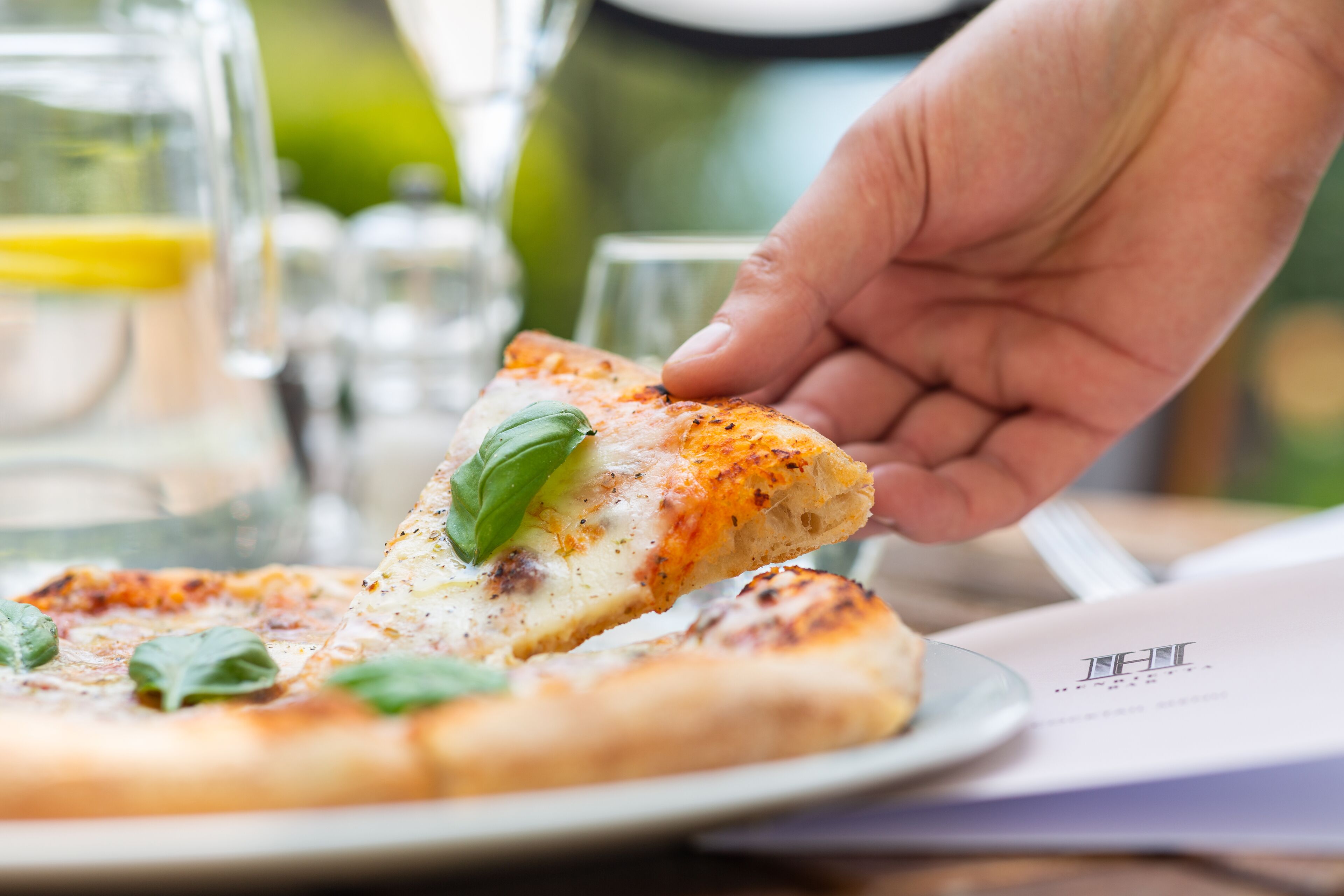 Une main tenant une part de pizza garnie de fromage et de feuilles de basilic.