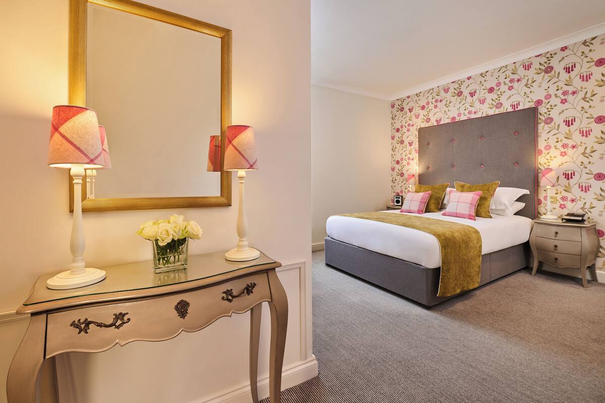 A bedroom with a large bed, a nightstand, a dresser, and a mirror.