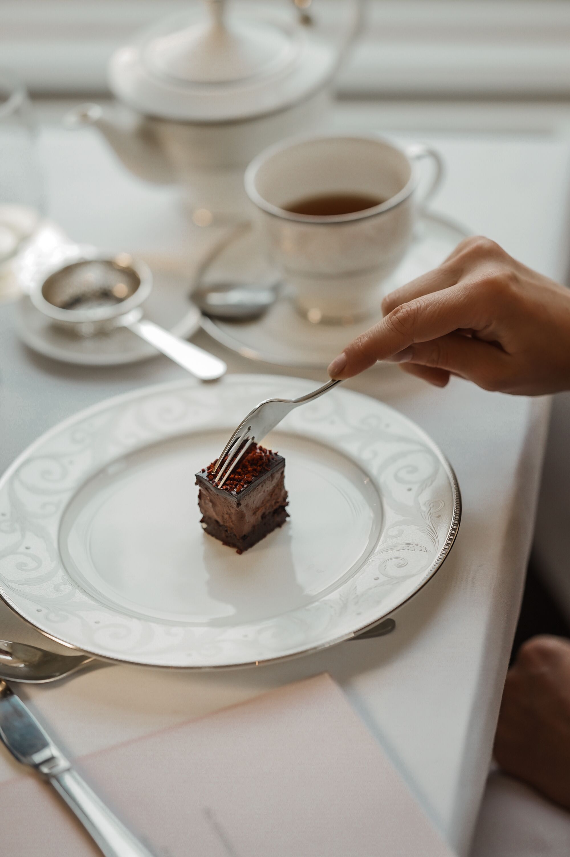 A close-up of a hand holding a fork with a piece of cake on a white plate.