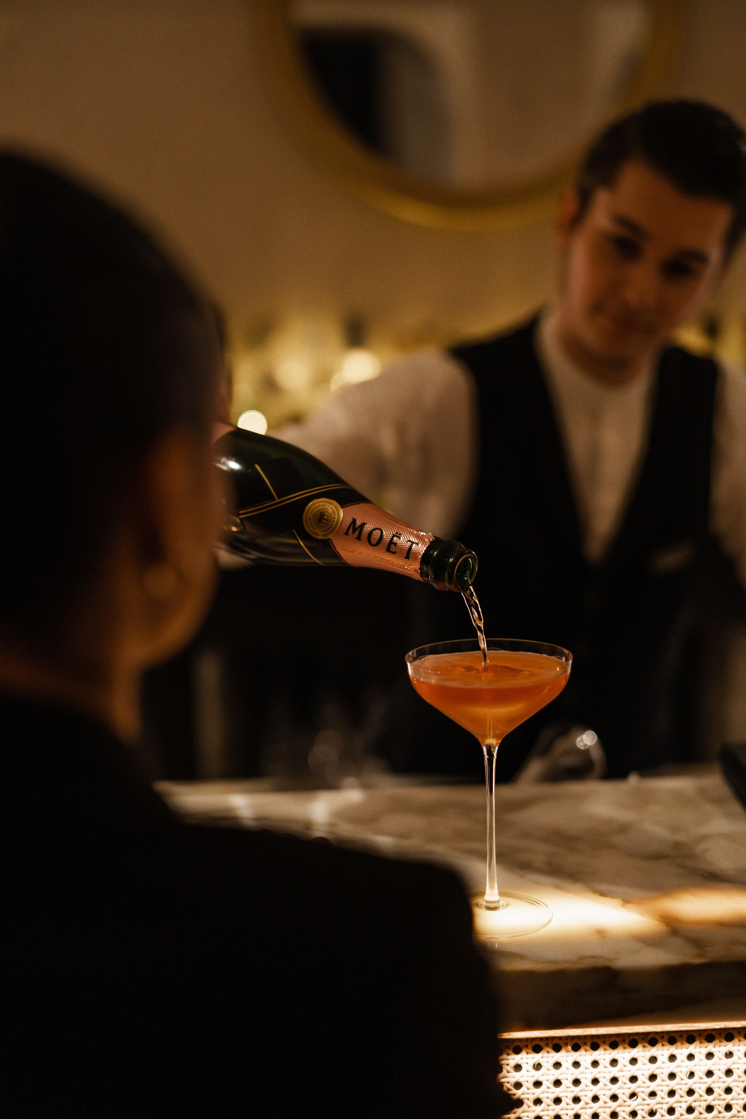 Une personne verse une boisson d’une bouteille portant l’étiquette « MO ËT » dans un verre à martini.