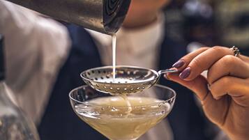 A bartender pouring a drink into a martini glass.