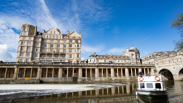 A historic building with classical architecture, a river, and a boat.