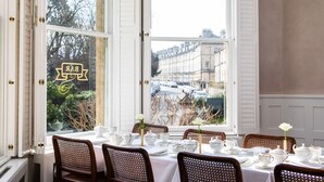 A dining area with a table set for four, white tablecloths, and chairs with a woven backrest.