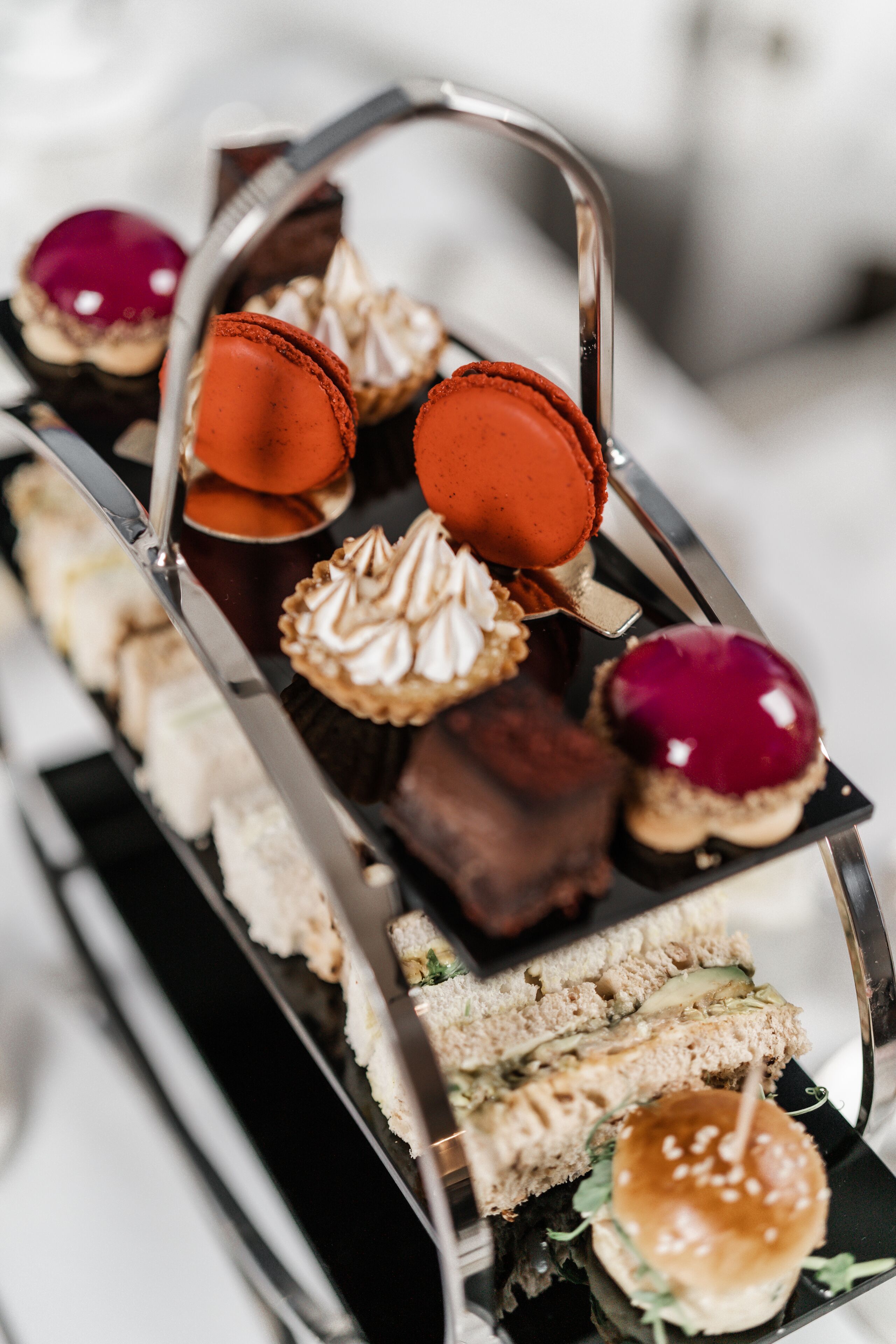 A tiered tray of assorted desserts including macarons, a sandwich, and a burger.