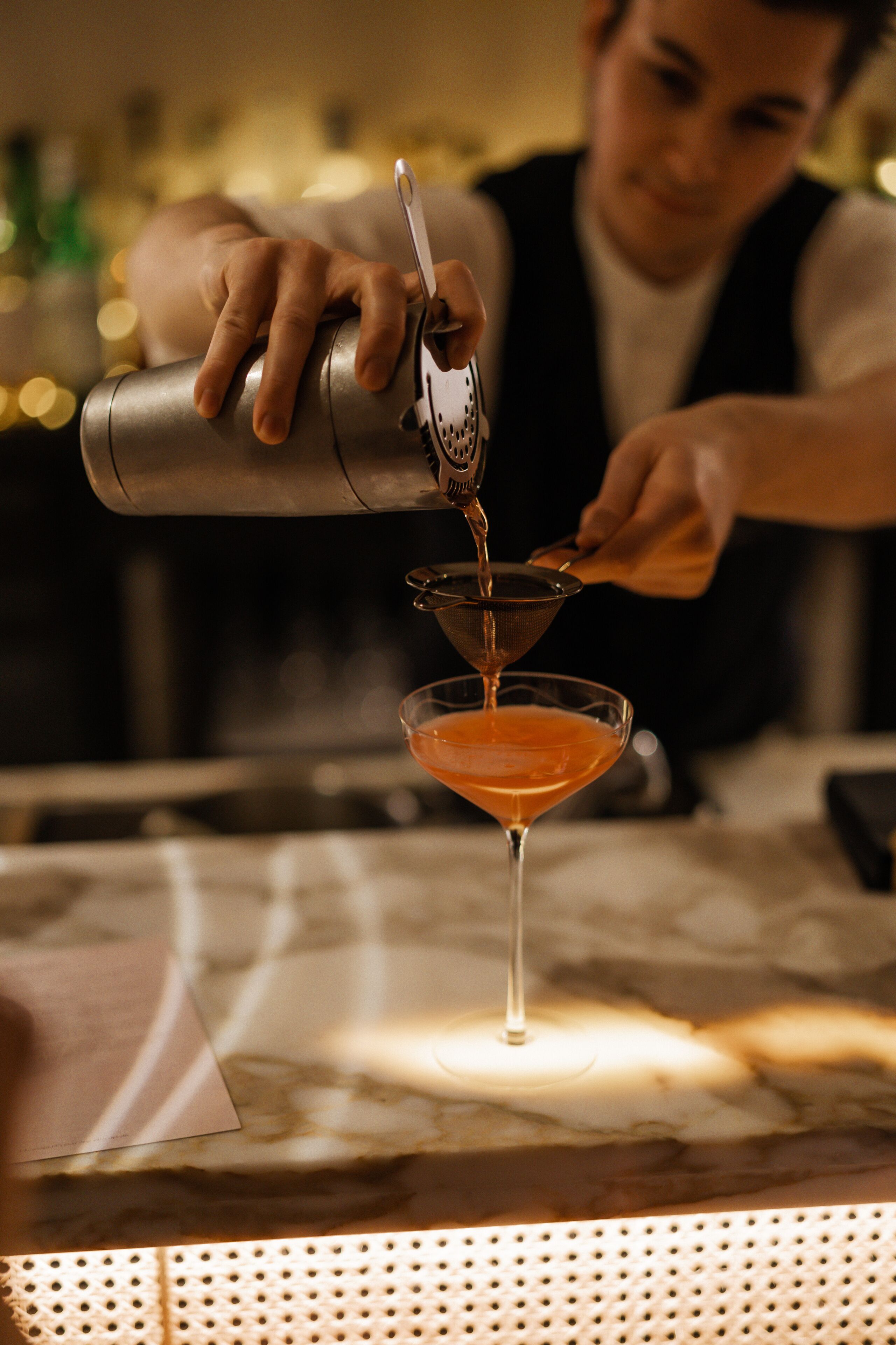 A bartender pouring a drink into a martini glass.