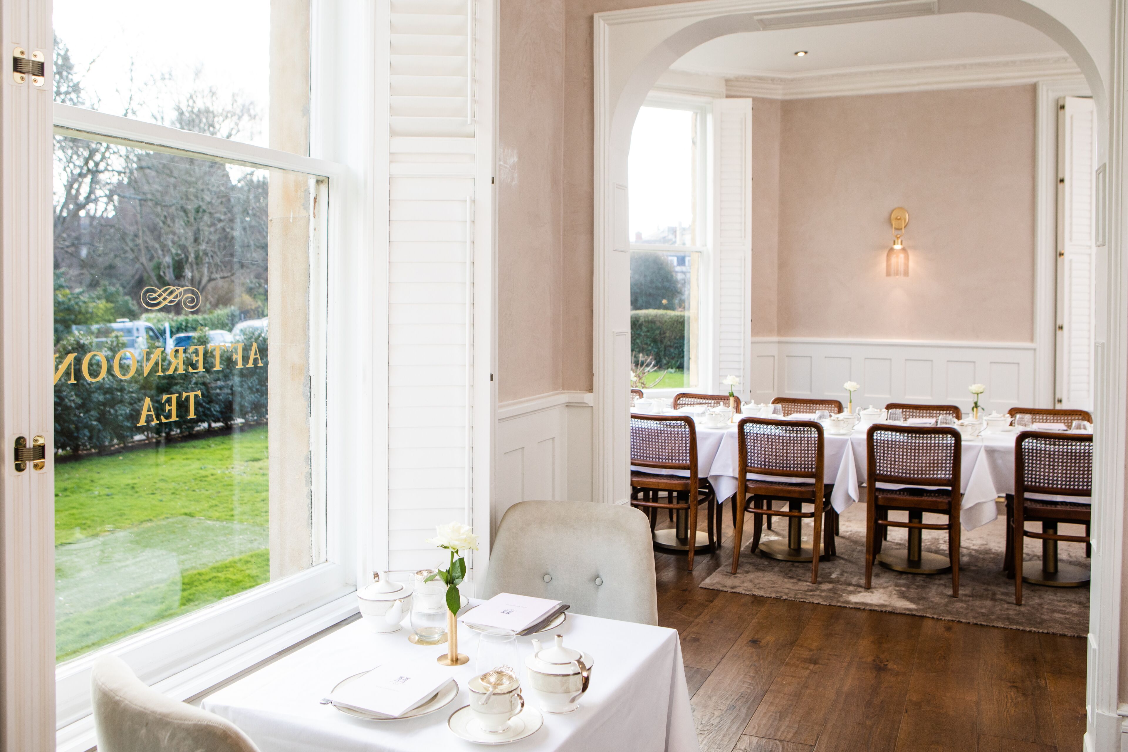 Un coin repas avec des tables dressées pour le repas, une vue sur un jardin par la fenêtre et un luminaire fixé au mur.
